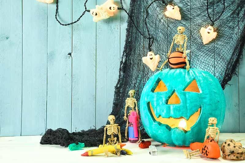 Horizontal image of a teal pumpkin on a table with other decor.