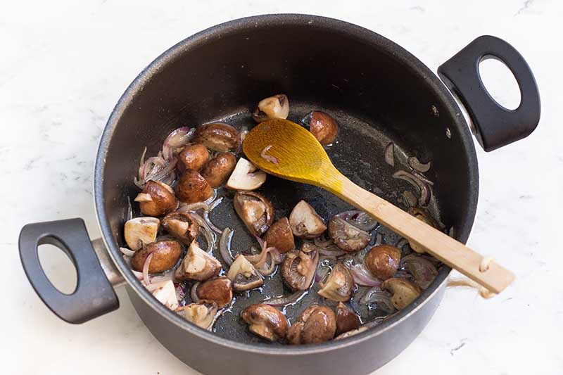 Horizontal image of cooking sliced mushrooms and shallots in a large pot.