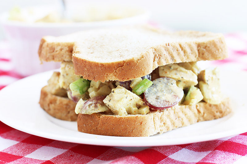 Horizontal image of a sandwich with a chicken, veggie, and grape filling.
