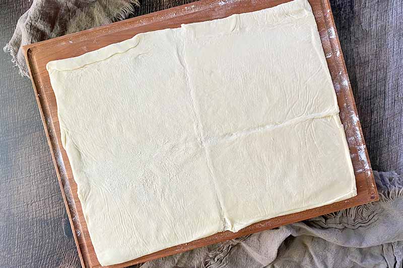Horizontal image of a sheet of dough on a large wooden cutting board.