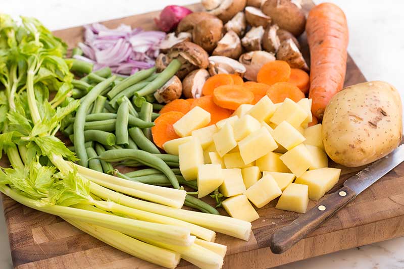 Horizontal close-up image of a wooden cutting board with prepped mixed vegetables.