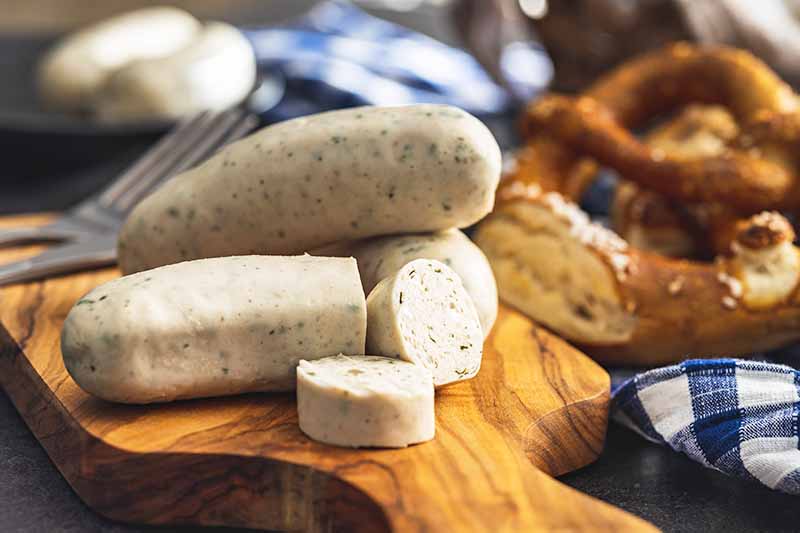 Horizontal image of Bavarian white meat links on a wooden board next to soft pretzels.