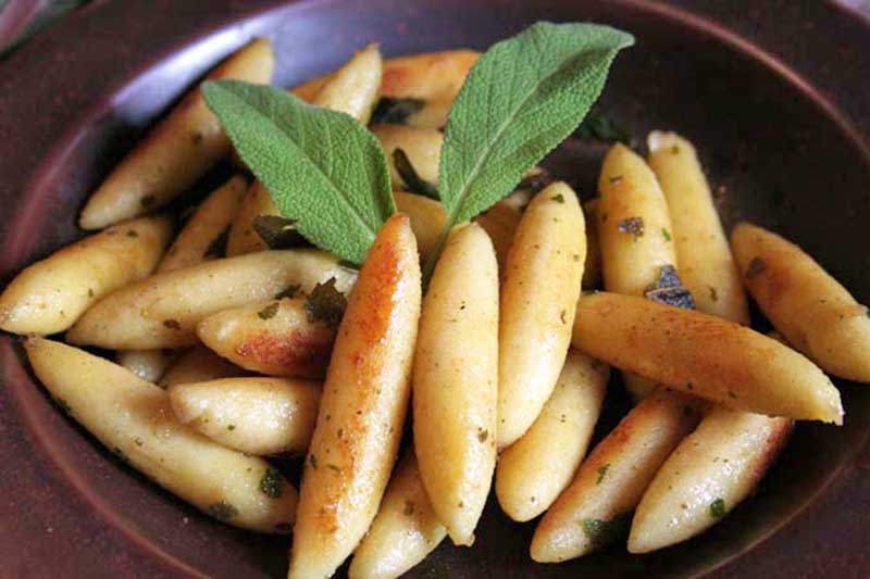 Horizontal image of a brown plateful of lightly caramelized potato dumplings with an herb garnish.