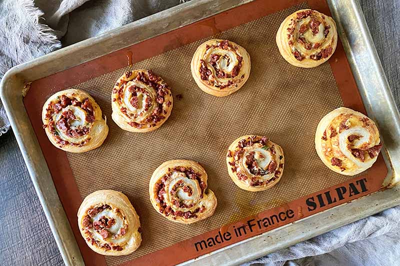Horizontal image of baked pinwheels on a sheet pan with a silicone mat.