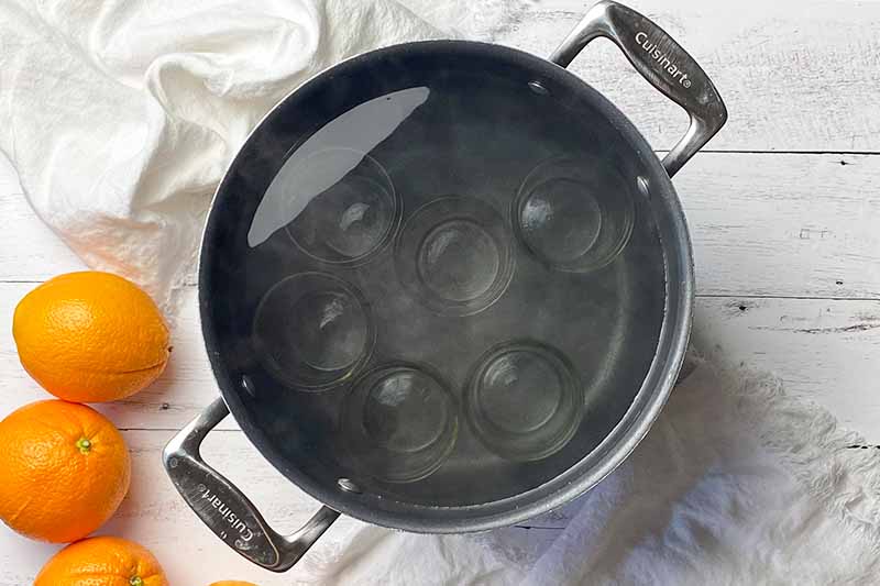 Horizontal image of sterilizing glass jars in a large pot of hot water.