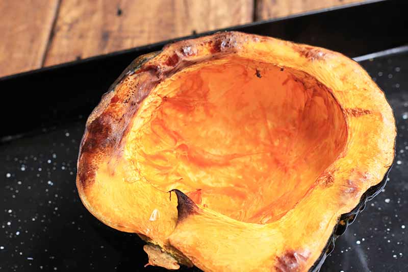 Horizontal image of half of a small squash roasted on a baking sheet pan.