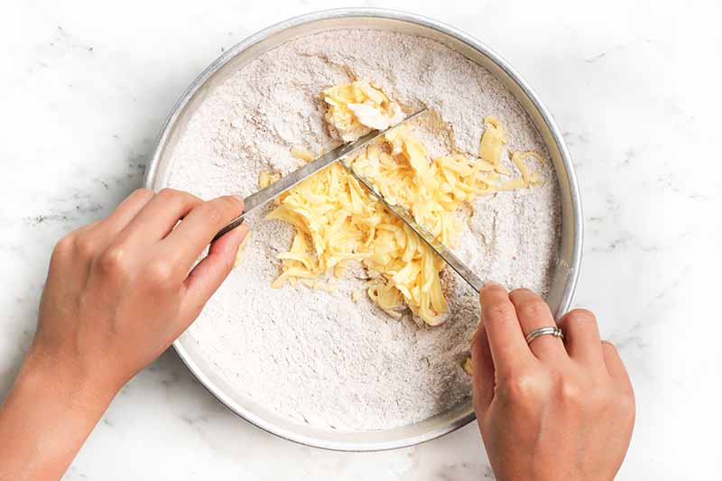 Horizontal image of cutting butter into flour in a large pan.