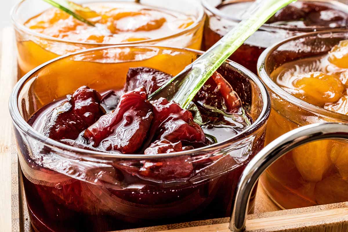 Horizontal image of chunky preserves in glass bowls with spoons.
