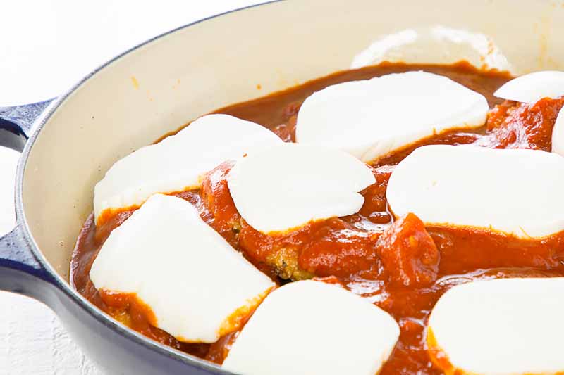 Horizontal image of fillets topped with tomato sauce and mozzarella cheese slices in a casserole dish.