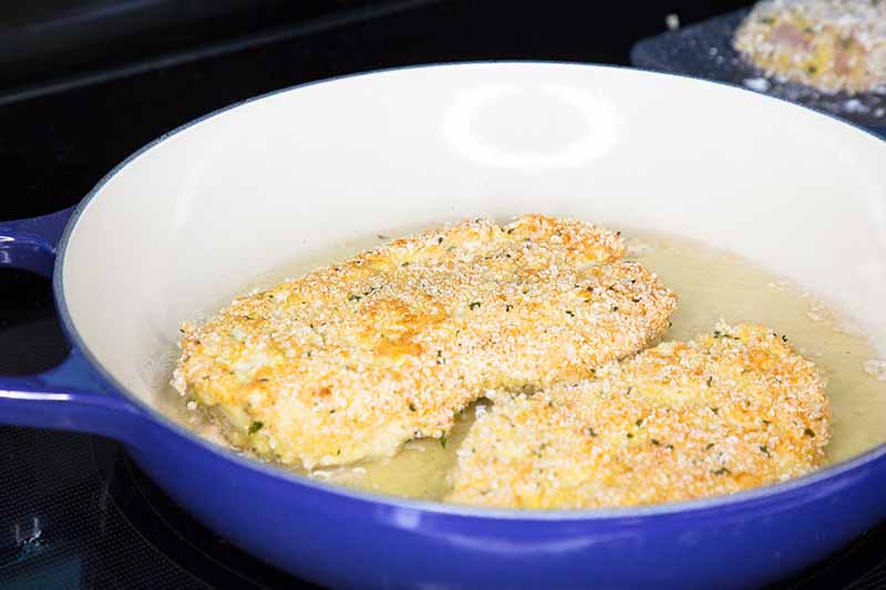 Horizontal image of searing breaded fillets in a large casserole dish on the stovetop.