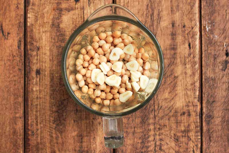 Horizontal image of a blender filled with garbanzo beans and slices of garlic.