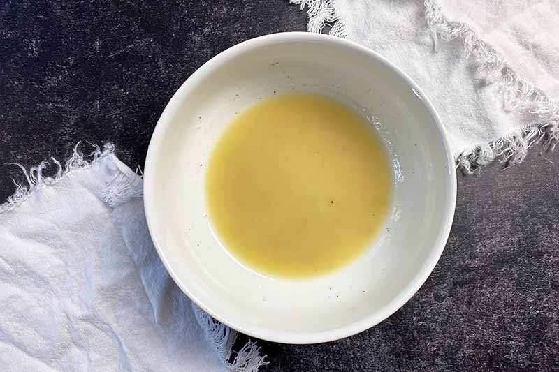 Horizontal image of a light yellow vinaigrette freshly made in a white bowl.