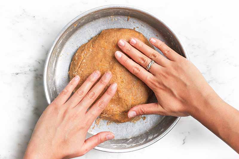 Horizontal image of hands molding dough into a circular shape.