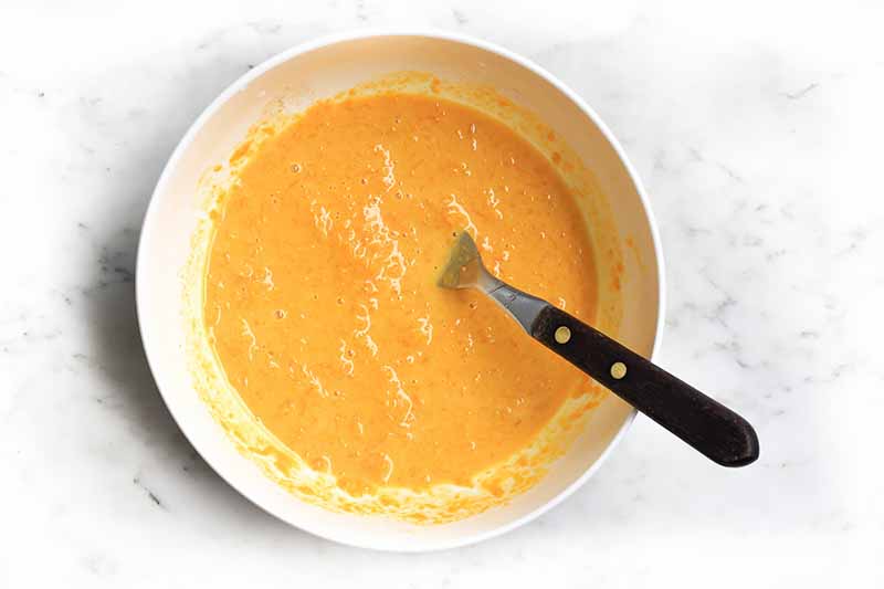 Horizontal image of an orange-colored wet mixture in a white bowl.
