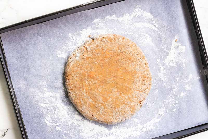 Horizontal image of a circular mound of dough on a sheet pan covered with parchment paper.
