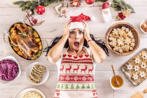 Horizontal image of a stressed out woman in a Christmas apron surrounded by Christmas food and decor.