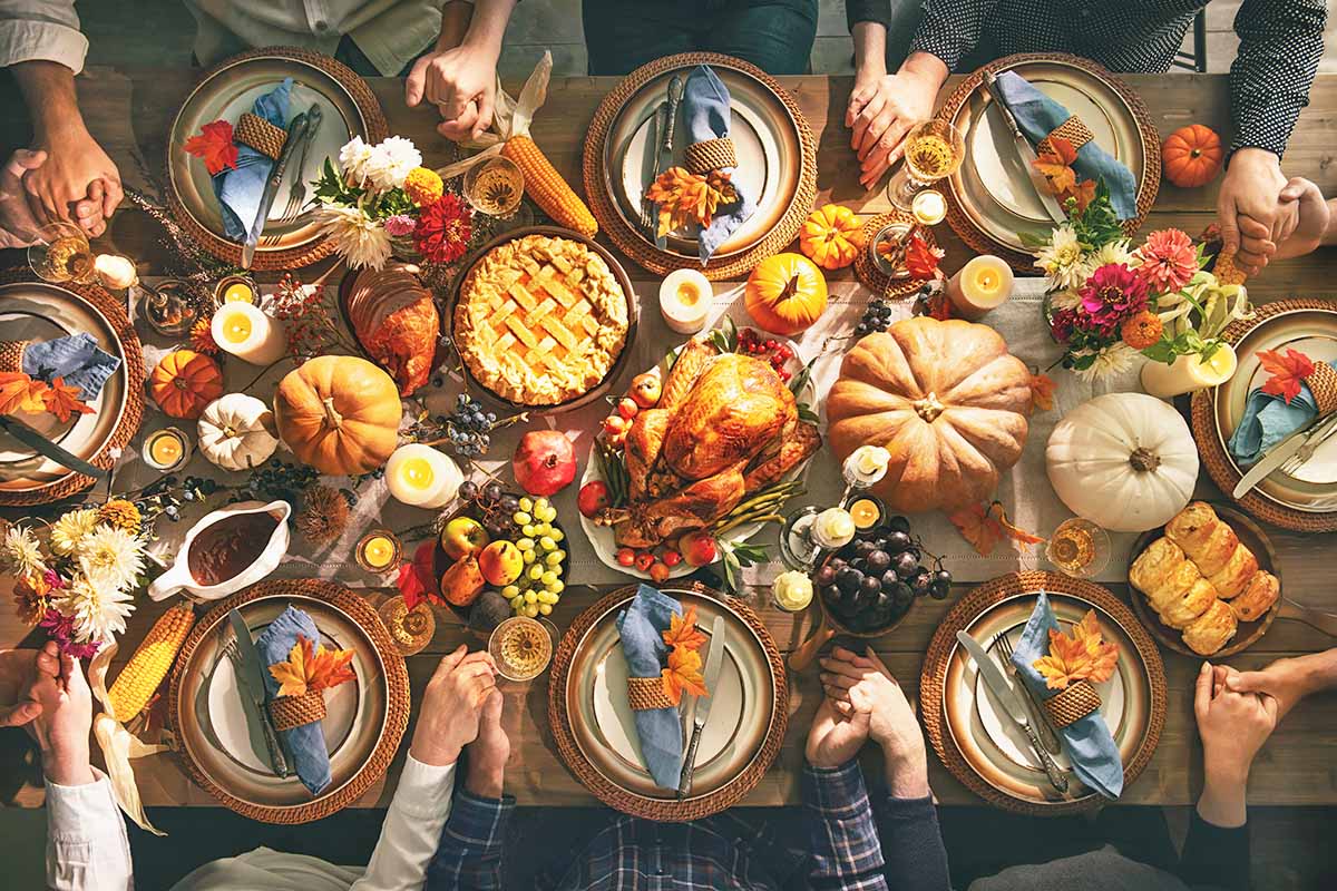 Horizontal image of a beautifully decorated fall feast, with family members holding hands.