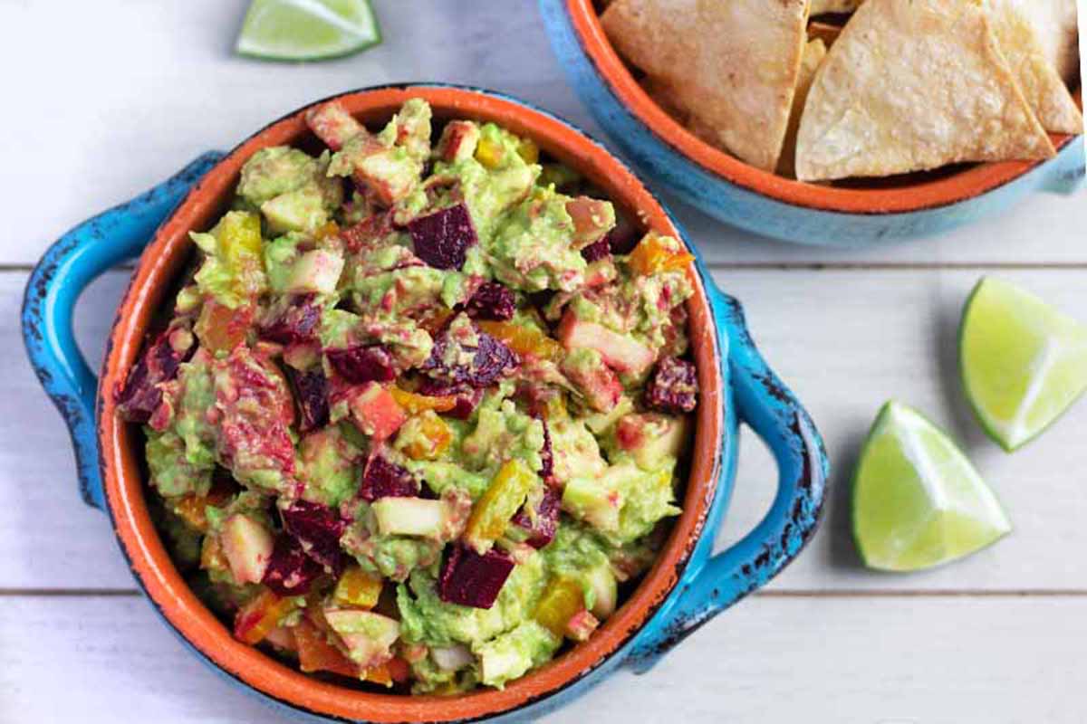 Horizontal image of a colorful guacamole next to tortilla chips and wedges of lime.