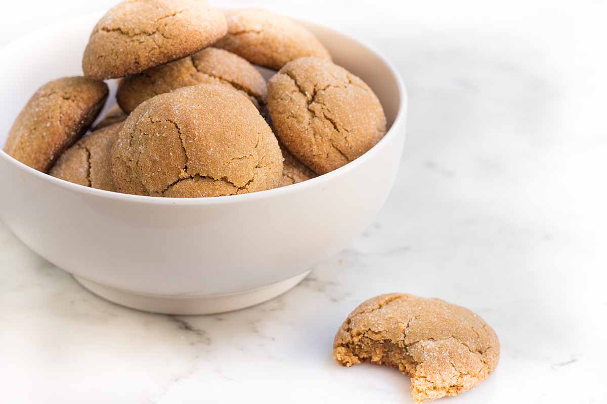 Horizontal image of a bowlful of sugar-coated cookies, with one on the marble counter with a bite taken out of it.