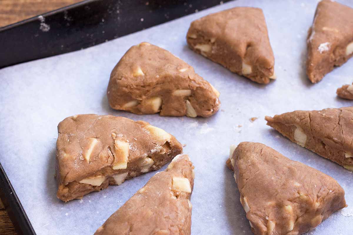 Horizontal image of unbaked triangular-shaped pastries on parchment paper on a baking sheet.