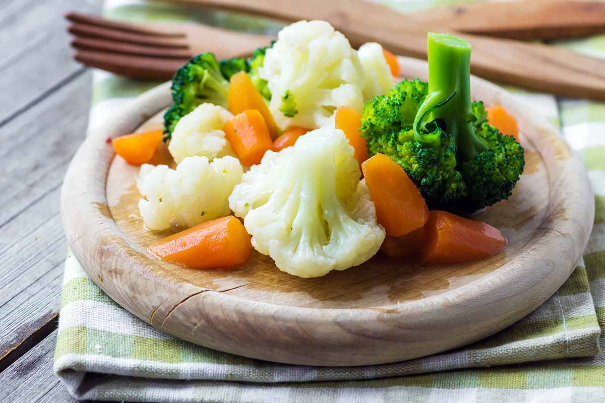 Horizontal image of steamed vegetables on a wooden plate.