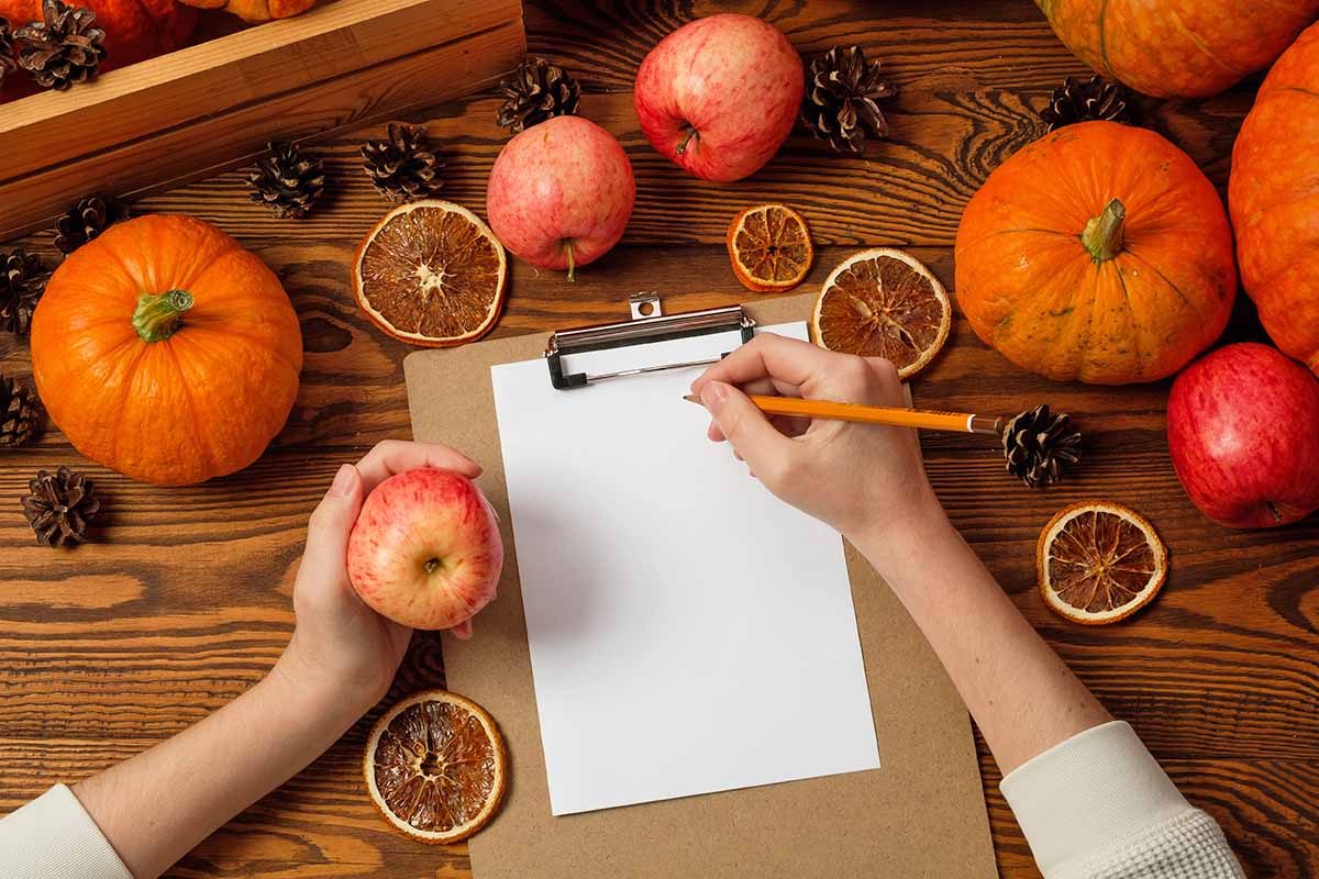 Horizontal image of preparing to write a list on paper next to fall-themed decor.
