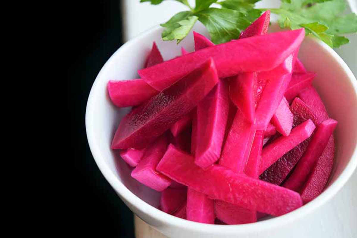 Horizontal image of a small dish with pink-hued pickles.