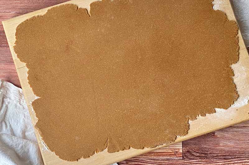 Horizontal image of flattened dough on a wooden cutting board.