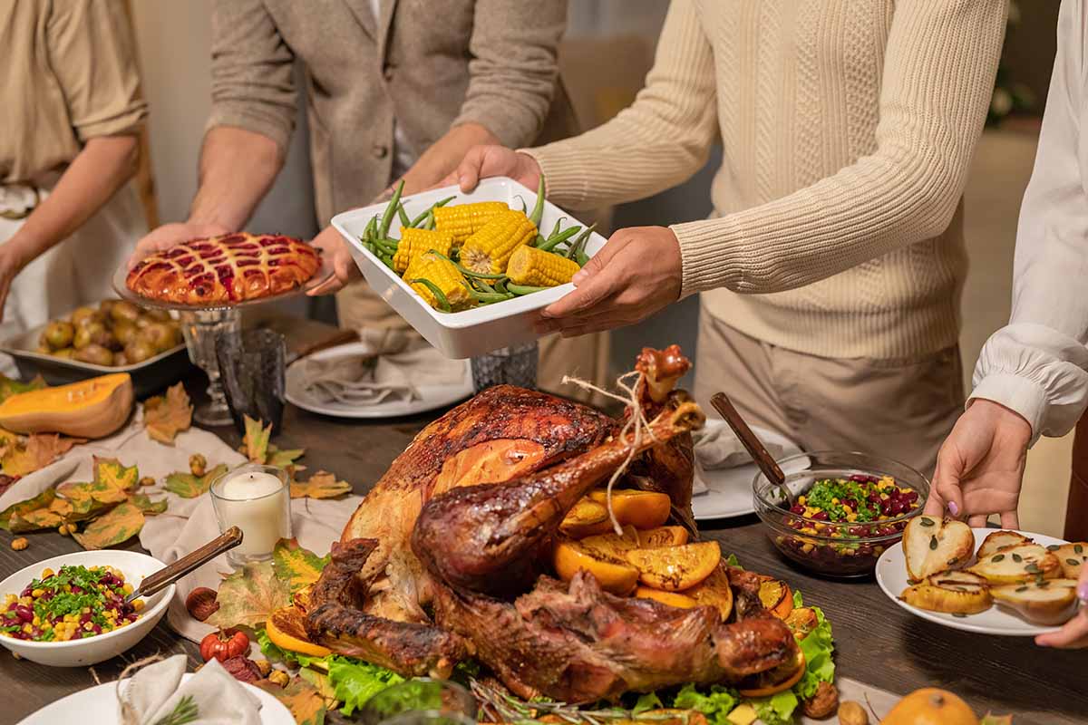 Horizontal image of four family members gathering holiday food on platters.