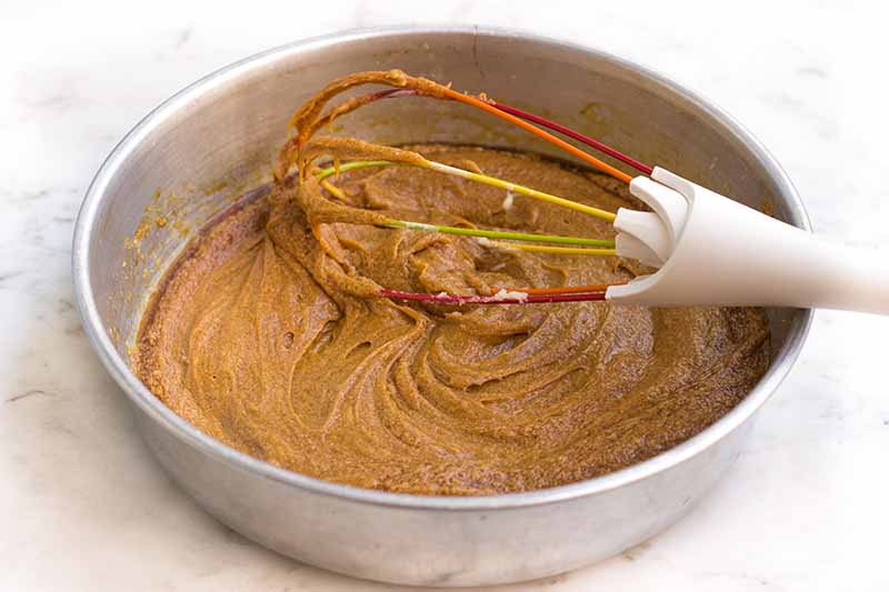 Horizontal image of whisking a molasses-flavored batter in a metal bowl.