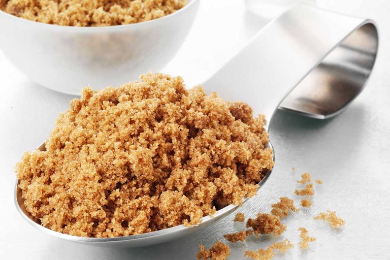 Horizontal image of a large spoonful and a bowlful of brown sugar.