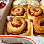 Horizontal close-up image of cranberry cinnamon rolls in a casserole dish, half of them frosted.