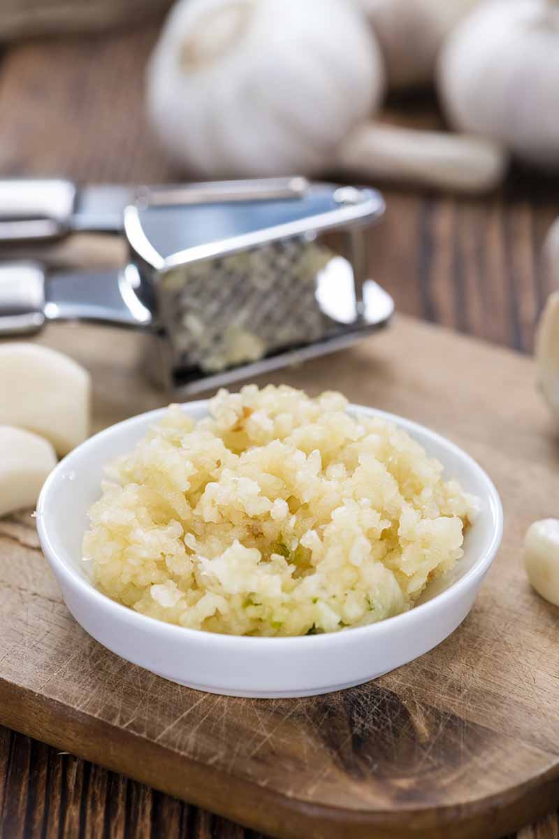 Vertical image of freshly minced garlic in a white plate on a wooden board.