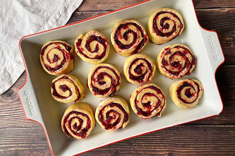 Horizontal image of rows of unbaked fruit-filled pastries in a casserole dish.