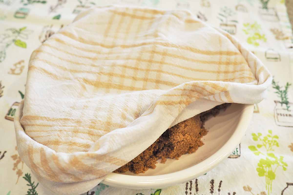 Horizontal image of a slightly damp towel over a white shallow bowl on tablecloth.
