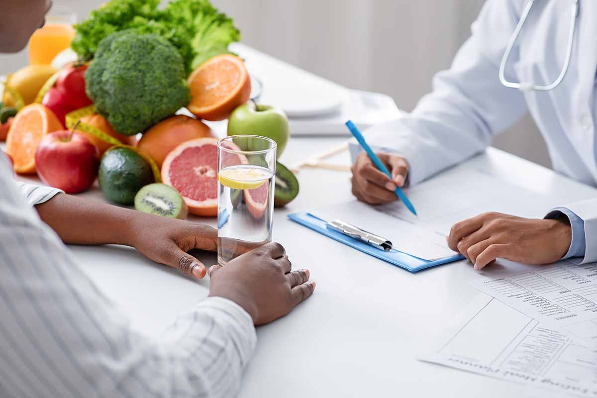 Horizontal image of a nutritionist and a client taking notes together next to a small mound of fresh and healthy ingredients.