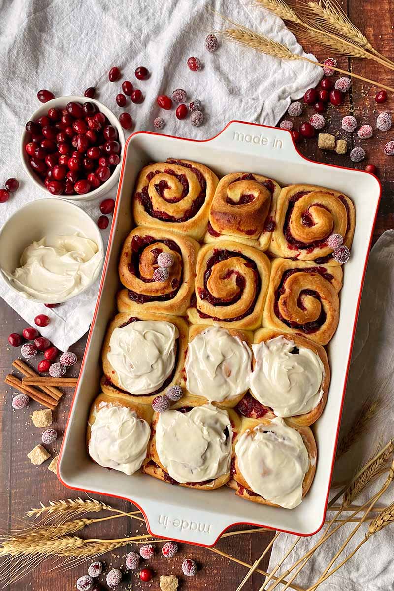 Vertical top-down image of freshly baked cinnamon rolls in a casserole dish, half of them covered in frosting.