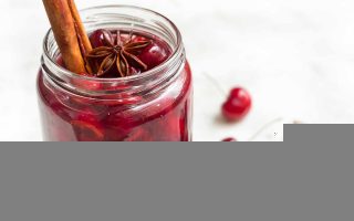 Horizontal image of a jar full of preserved cherries in syrup topped with a stick of cinnamon and star anise.