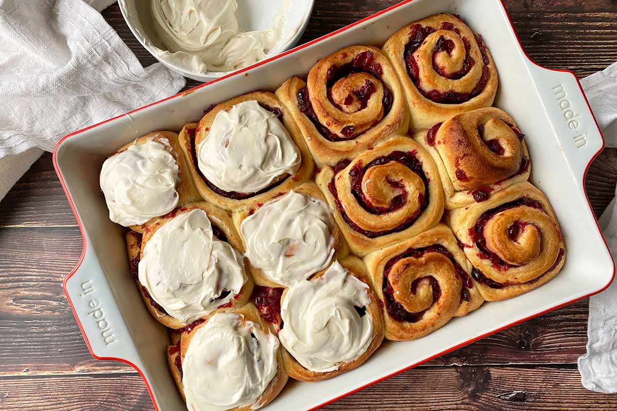 Horizontal image of freshly baked pastry pinwheels in a casserole dish, with half of them frosted.