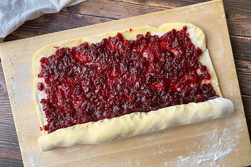Horizontal image of preparing a rolled pastry with a cranberry sauce spread.