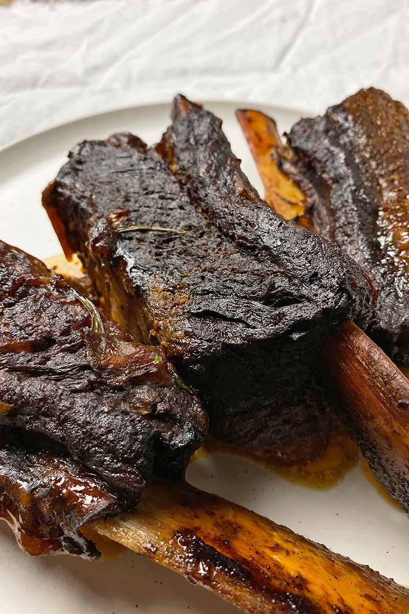 Vertical image of cooked whole, bone-in short ribs on a white plate.