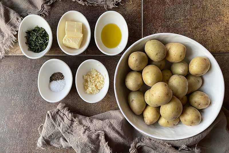 Horizontal image of measured ingredients in small bowls and washed baby spuds in a large white bowl.