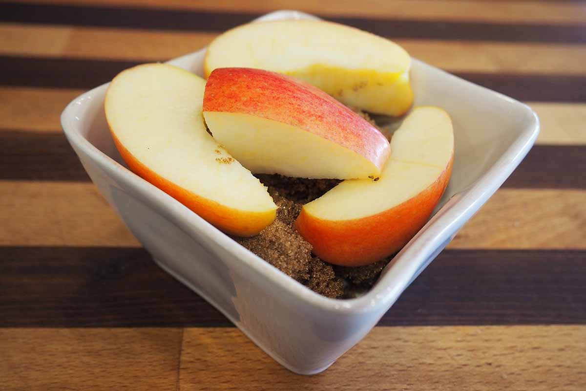 Horizontal image of thick apple slices in a square white bowl.