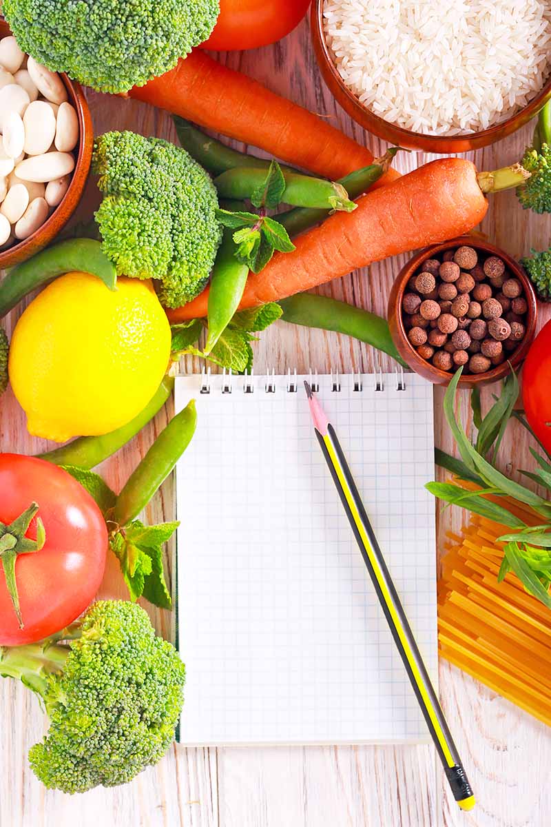 Vertical image of fresh and healthy food items surrounding a notepad and pencil.