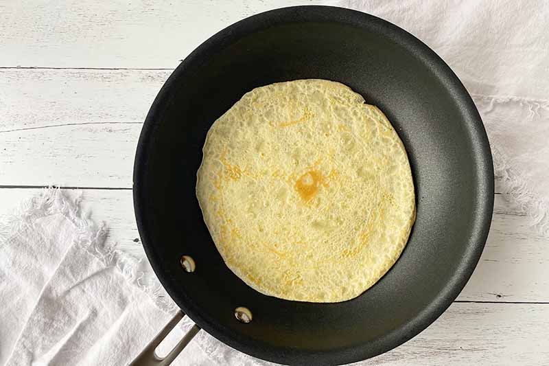 Horizontal image of cooking a very thin pancake in a nonstick skillet.