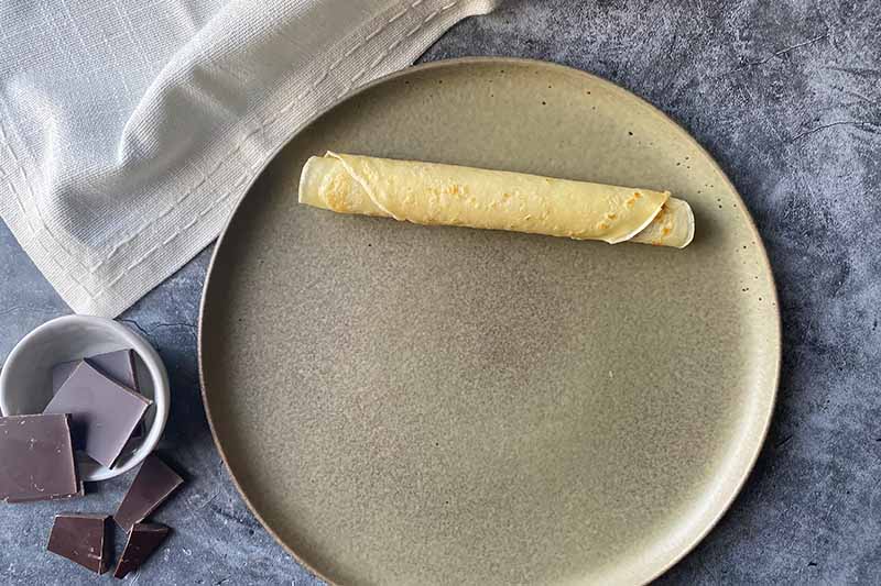 Horizontal image of a fully assembled filled and rolled crepe on a plate.