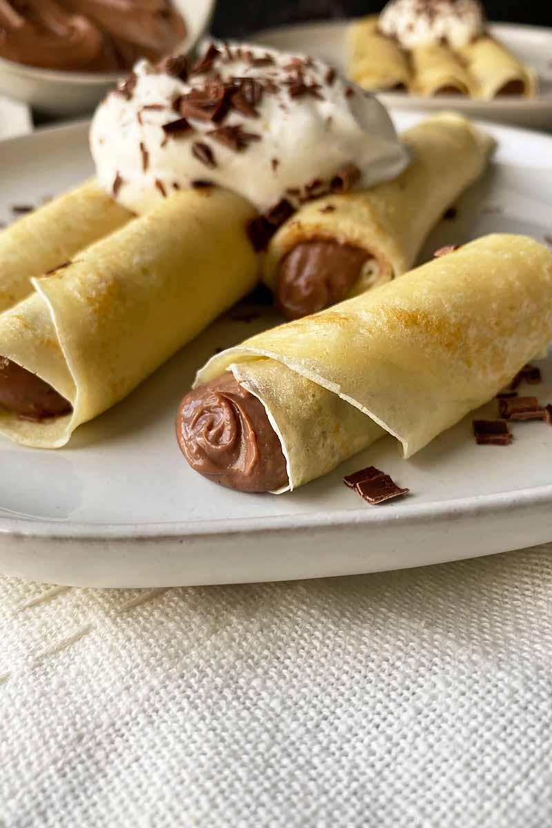 Vertical image of a halved crepe filled with a chocolate pudding on a white plate.