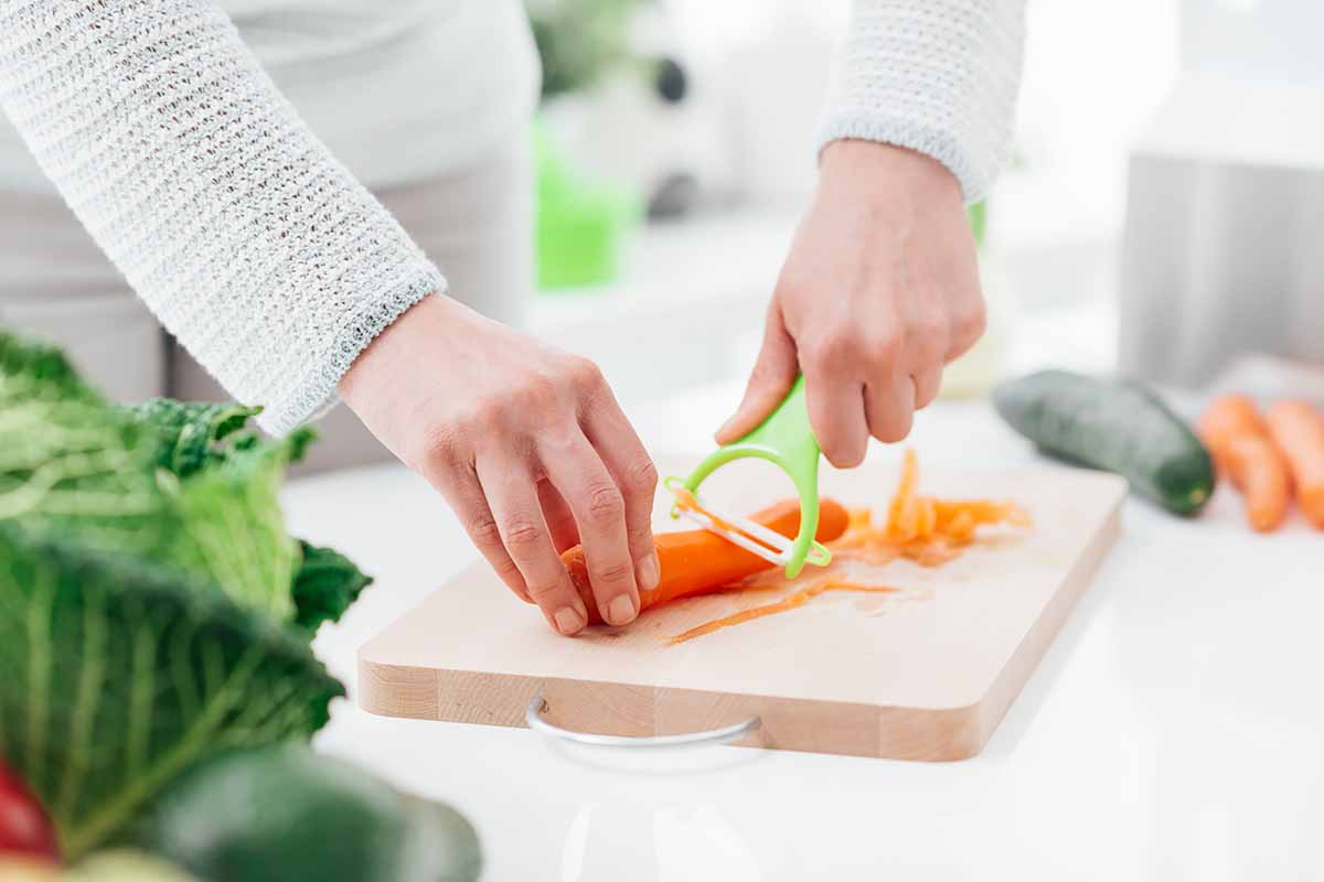 Horizontal image of a woman cleaning raw carrots on a wooden cutting board.