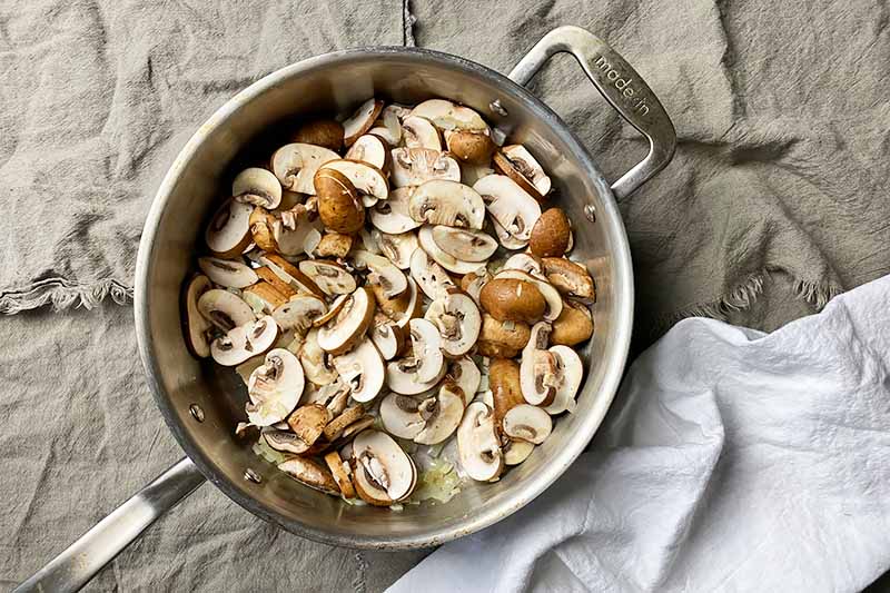 Horizontal image of cooking raw sliced mushrooms in a large skillet.