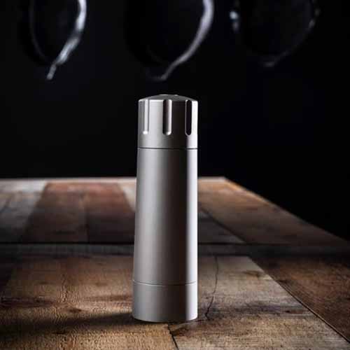 Image of the Mannkitchen Salt Cannon on a wooden table with a dark, black background.